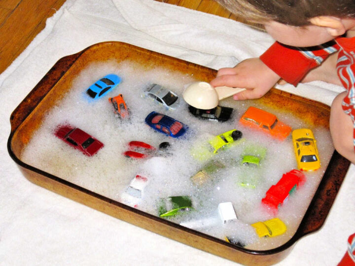Child playing with toy cards in bubble water in baking dish