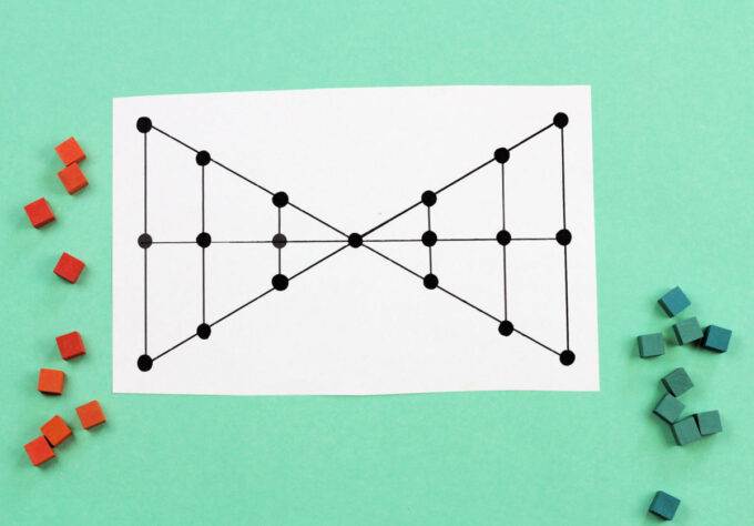 Lau kata kati  game board in shape of two triangles connected at a single vertex and bisected by one horizontal and four vertical lines. Nine orange tokens and nine green tokens off to the side