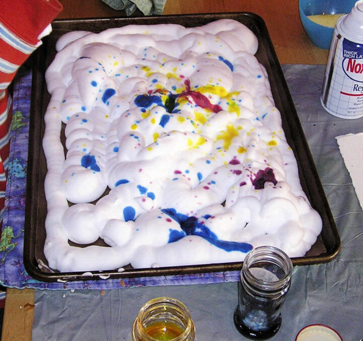 Drops of red, blue and yellow liquid watercolor on shaving cream in tray