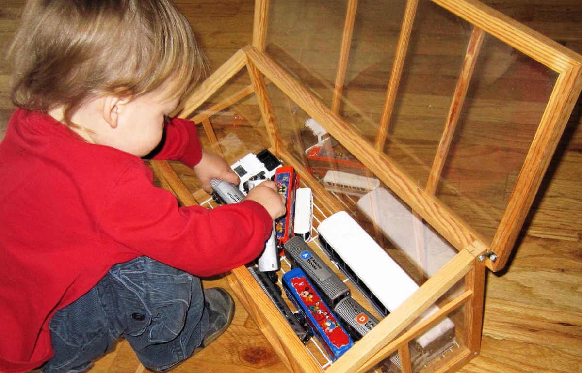child playing with toy vehicles in small indoor greenhouse