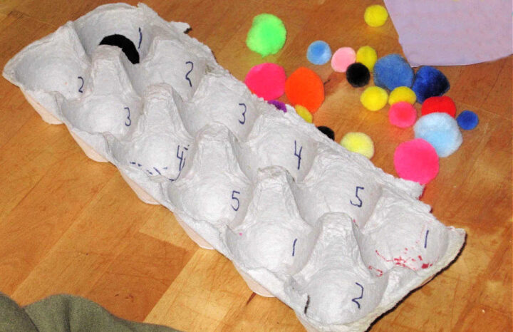 Empty egg carton with pile of pom poms