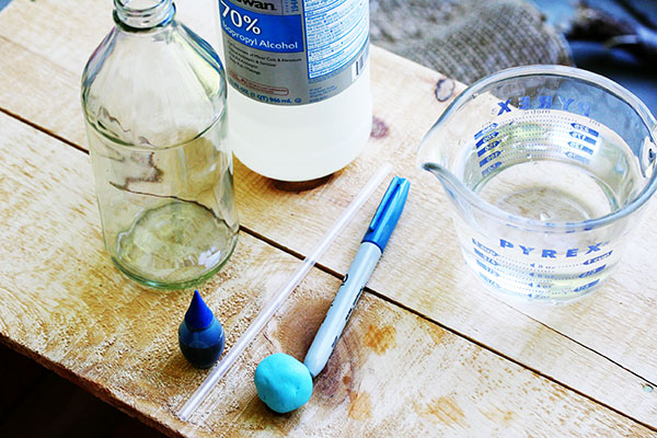 Materials for homemade thermometer science project: marker, glass bottle, water in measuring cup, straw, clay and marker.